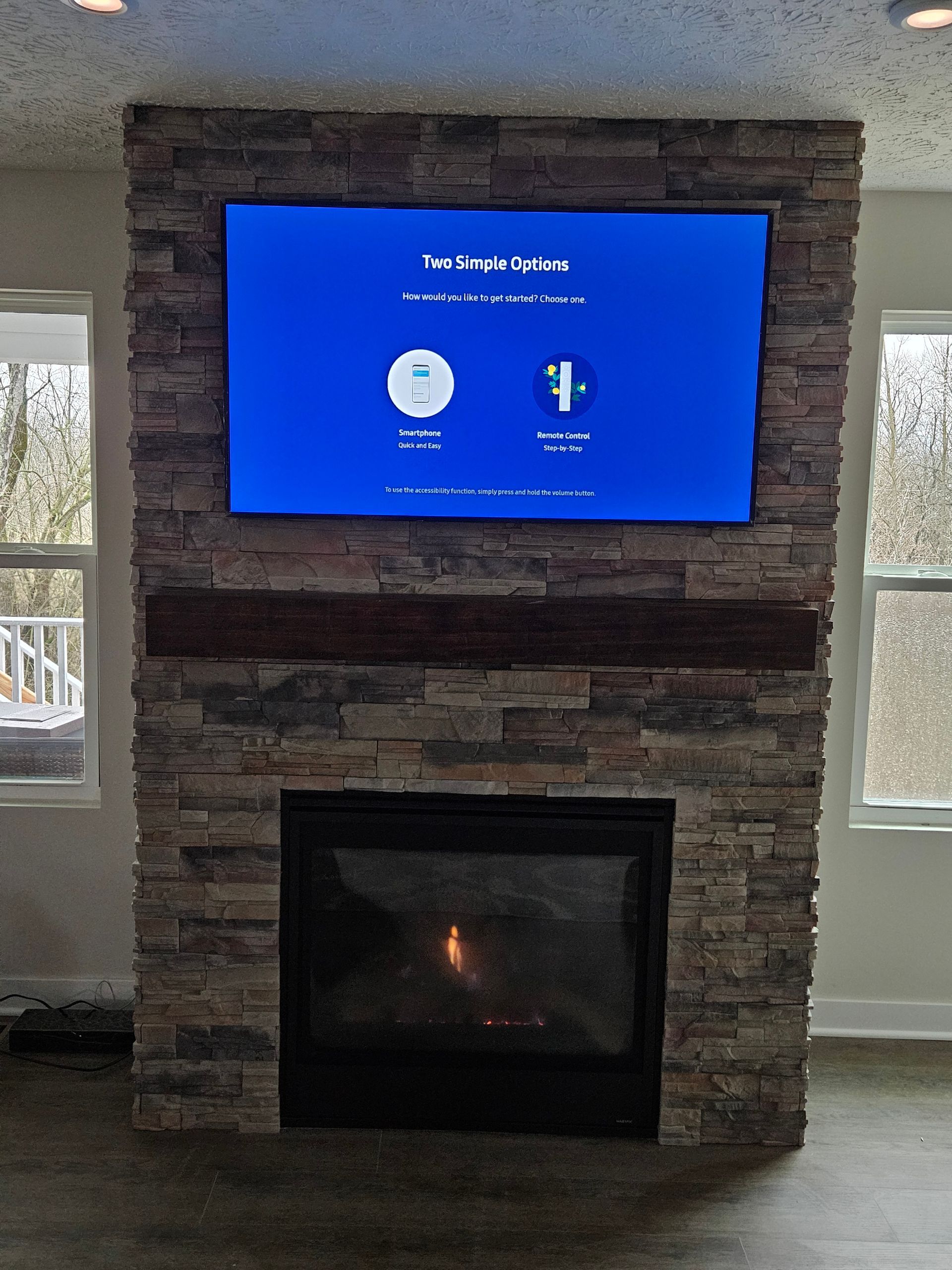 Living room stone fireplace with a wall-mounted TV showing a blue menu screen above the firebox