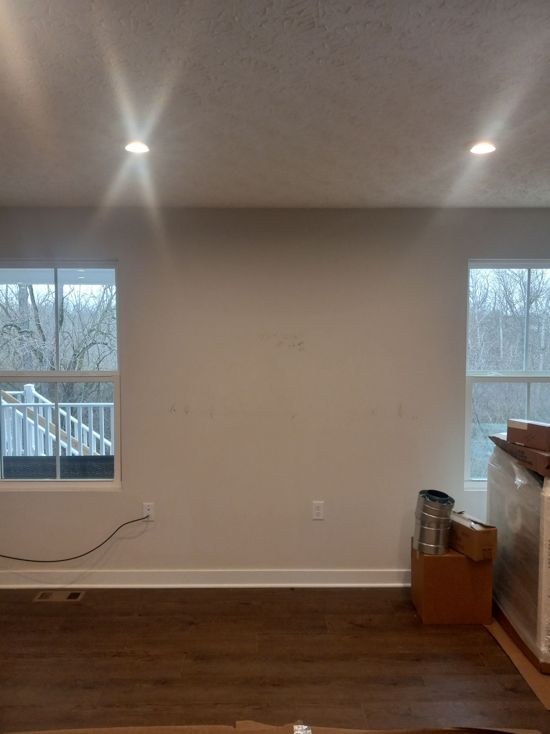 Empty living room with two windows, recessed lights, hardwood floor, and a fireplace on the right.
