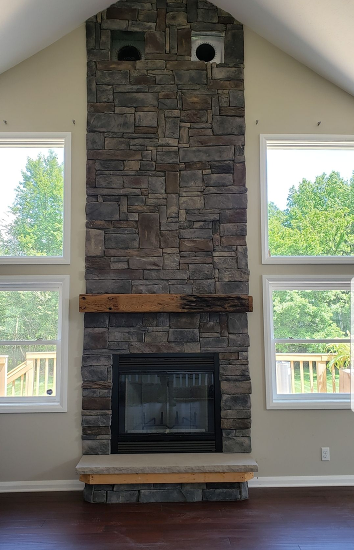 Stone fireplace wall with black firebox, wooden mantel, and two windows on either side.