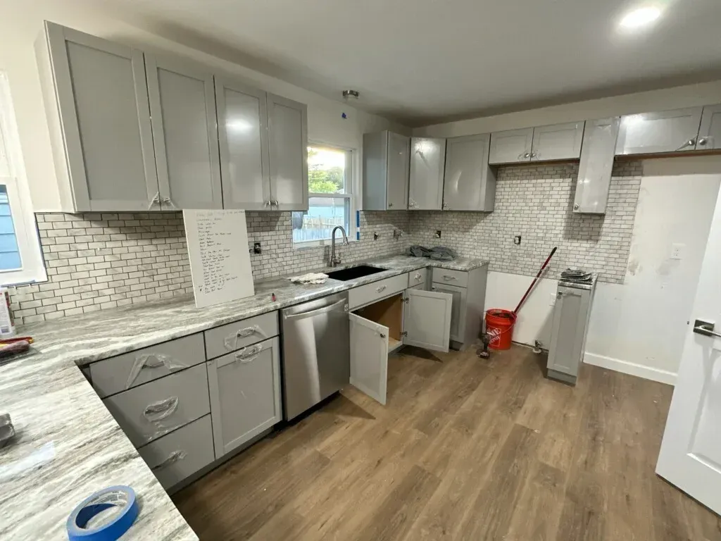 Modern kitchen with gray cabinets, white appliances, wood floors, and a window over the sink.