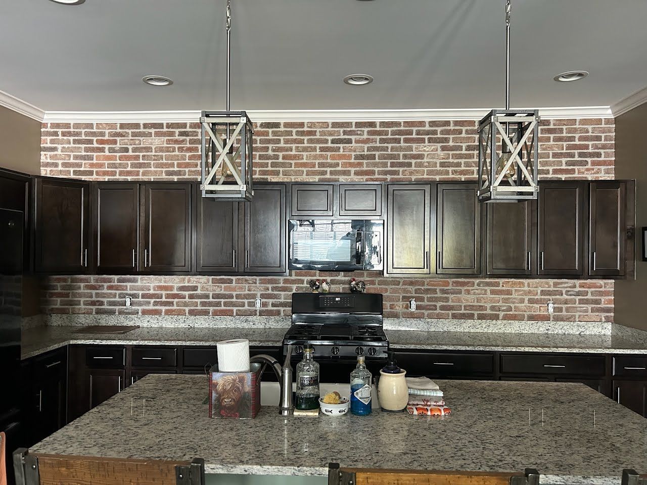Modern kitchen with brick backsplash, dark cabinets, granite island, and pendant lights