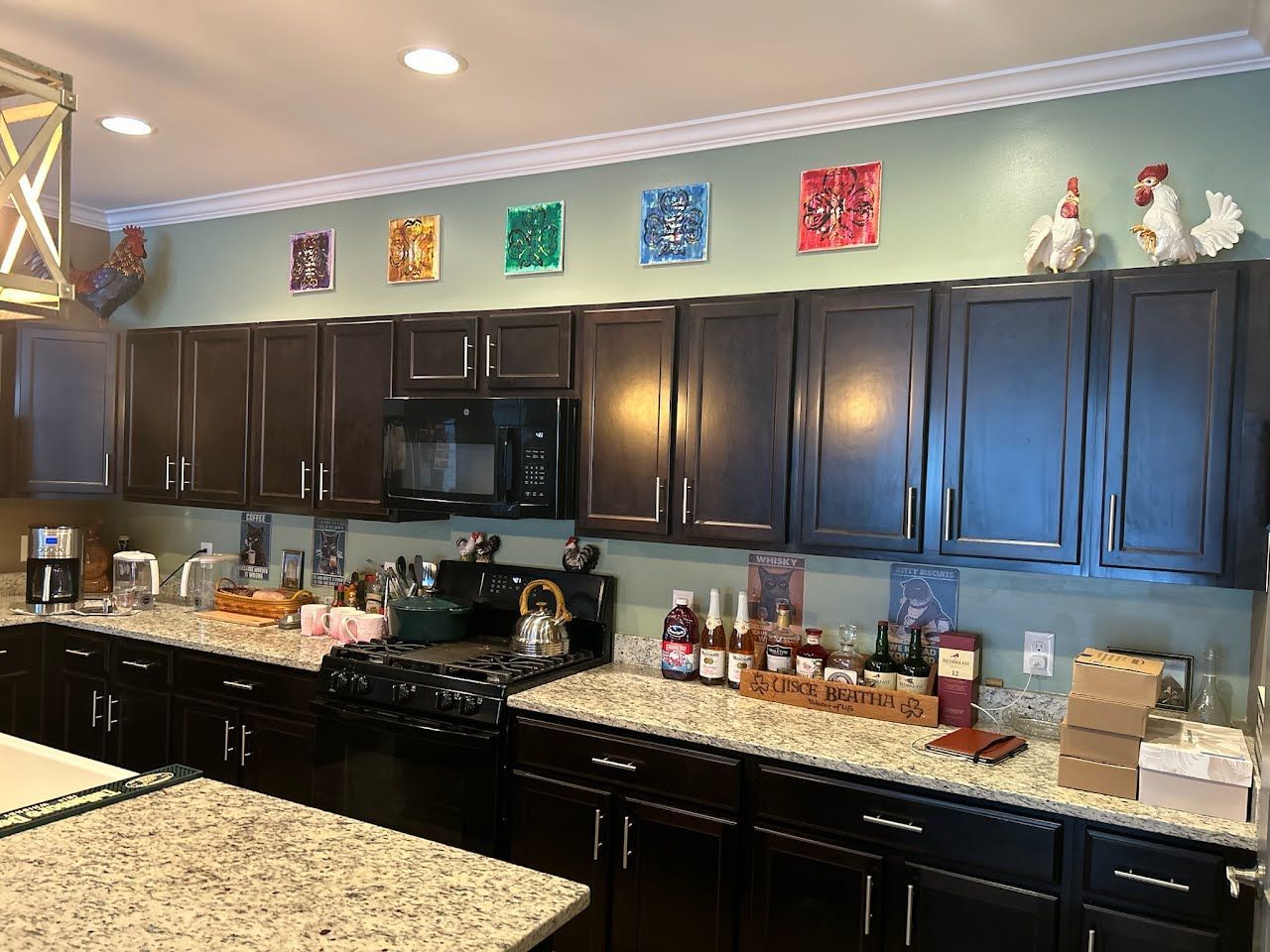 Kitchen with dark wood cabinets, granite countertops, and colorful wall art above the cabinets.
