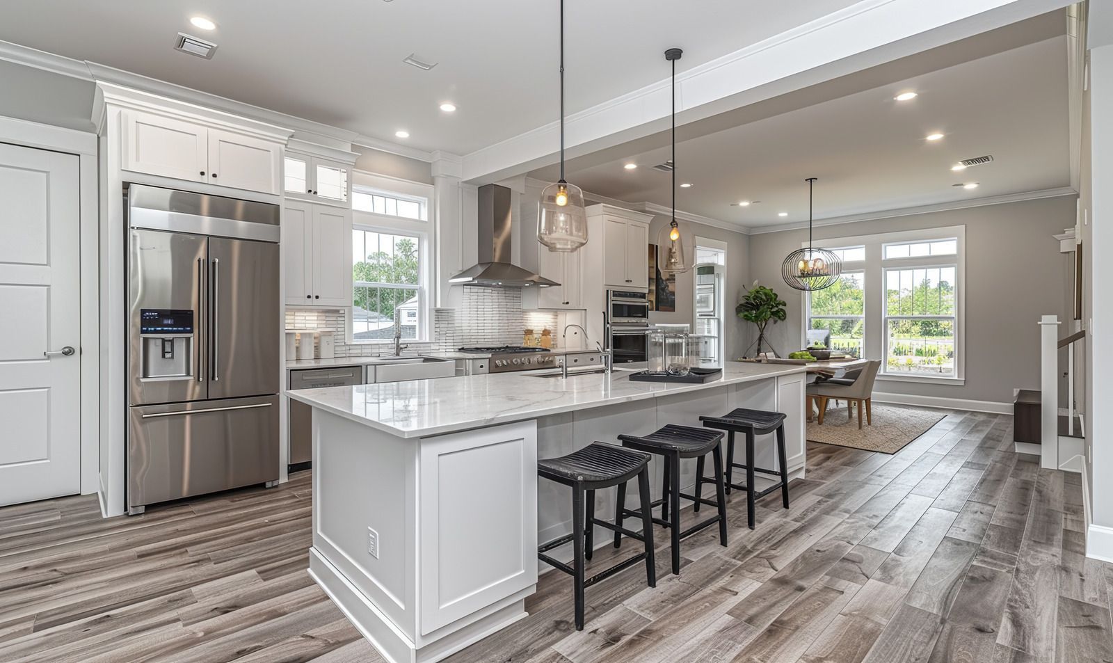 Bright modern kitchen with stainless steel appliances, large island, and pendant lights leading to a dining area.
