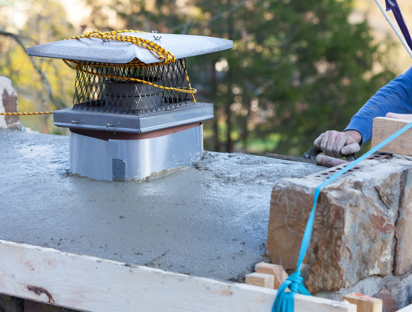 Concrete rooftop chimney cap with wire mesh and a person's hand beside it