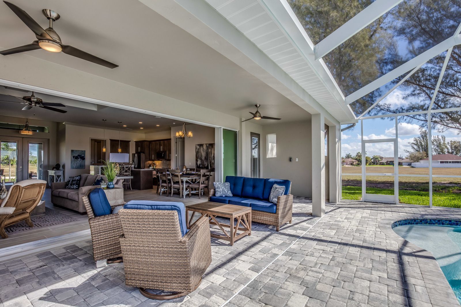 Covered patio with wicker seating, blue cushions, ceiling fan, and pool beside a sunny backyard.