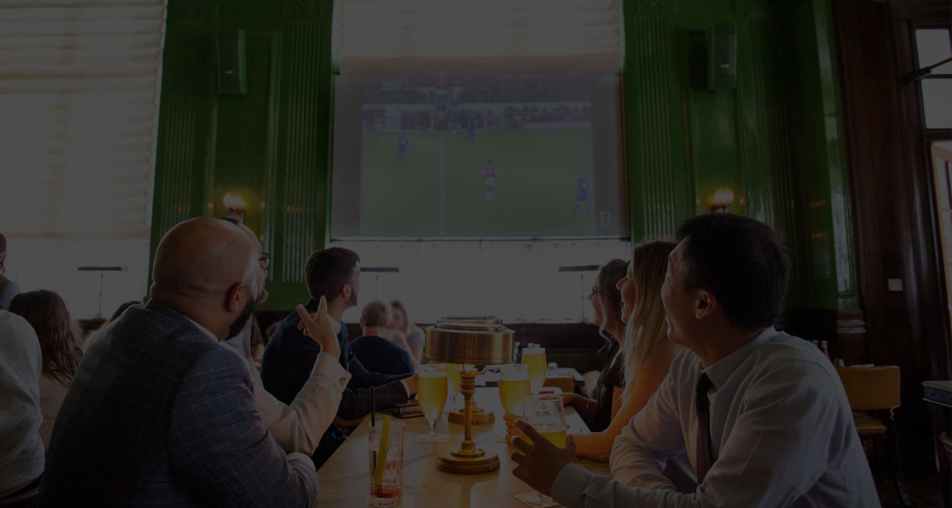 People seated at a restaurant watching a soccer match on a large screen.