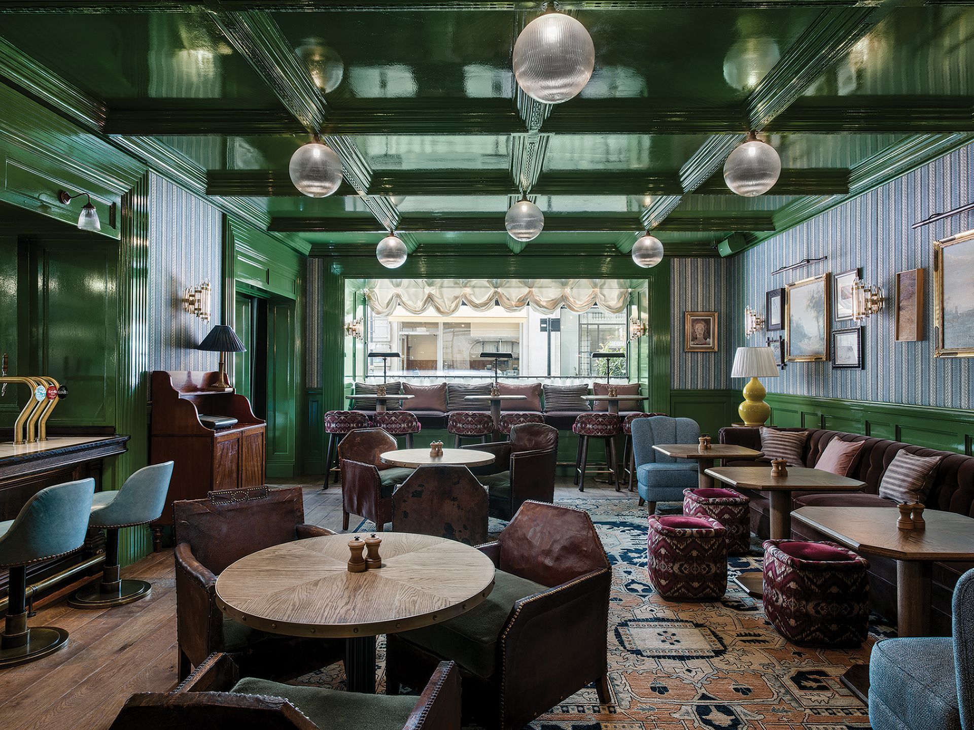 Green, mirrored lounge with velvet chairs, round tables, and hanging disco balls.