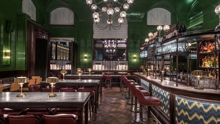 Elegant vintage bar and restaurant with green walls, red chairs, marble tables, and hanging globe lights