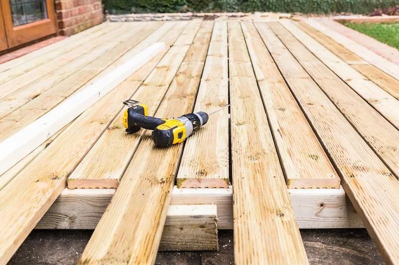 A drill is sitting on top of a wooden deck.