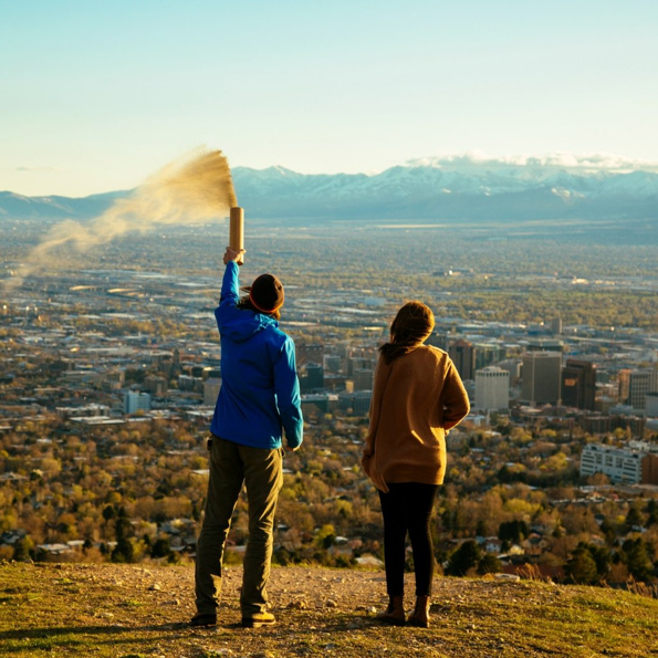 A man and a woman are standing on top of a hill overlooking a city.