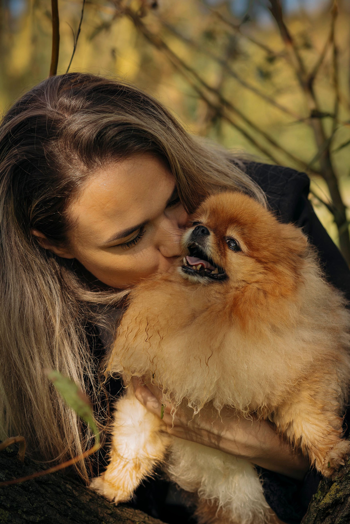 Iemand leunt met zijn voorhoofd tegen een grijze, gevlekte hond met open bek, waarmee een moment van stille verbondenheid wordt vastgelegd.