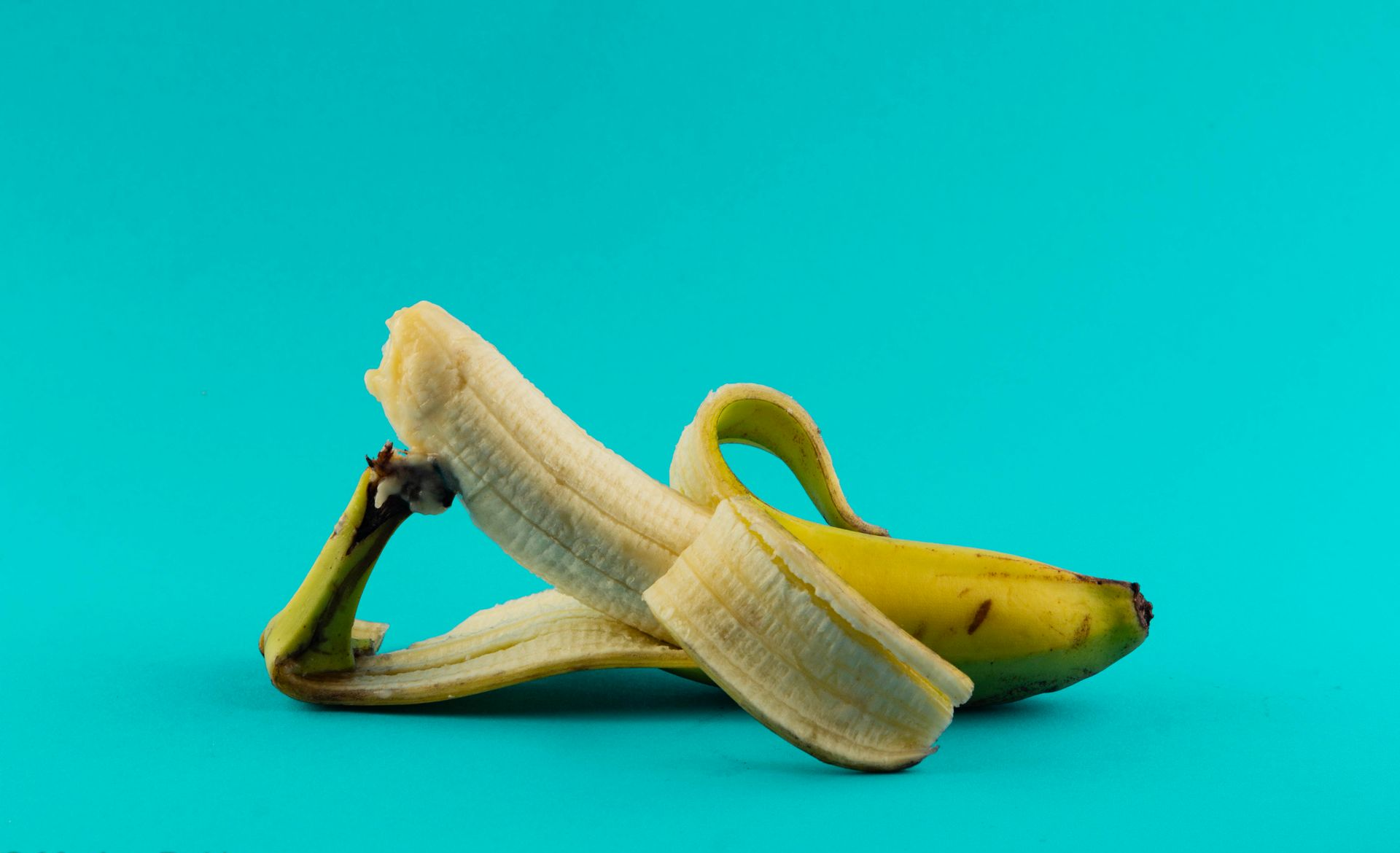 Een gedeeltelijk geschilde banaan op een turquoise achtergrond.