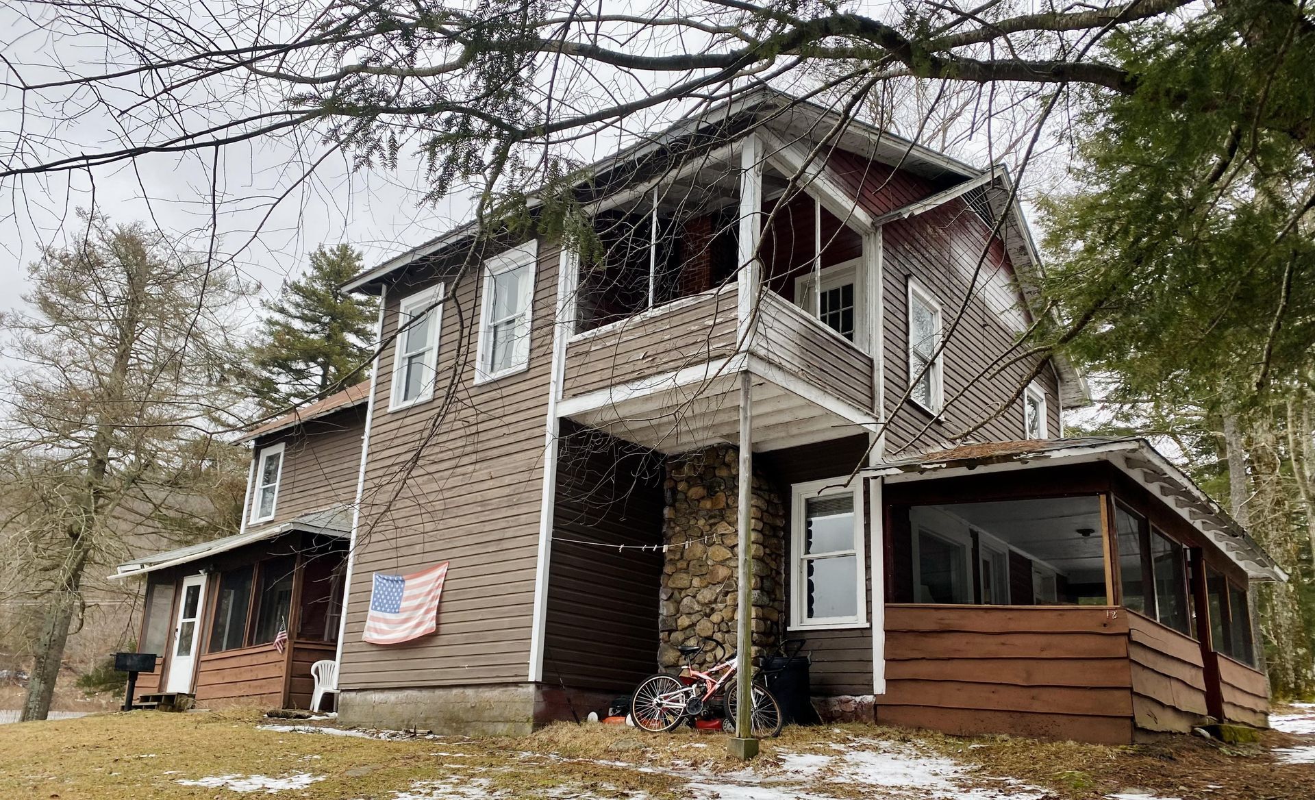 A large house with a porch and an american flag hanging on the side of it.