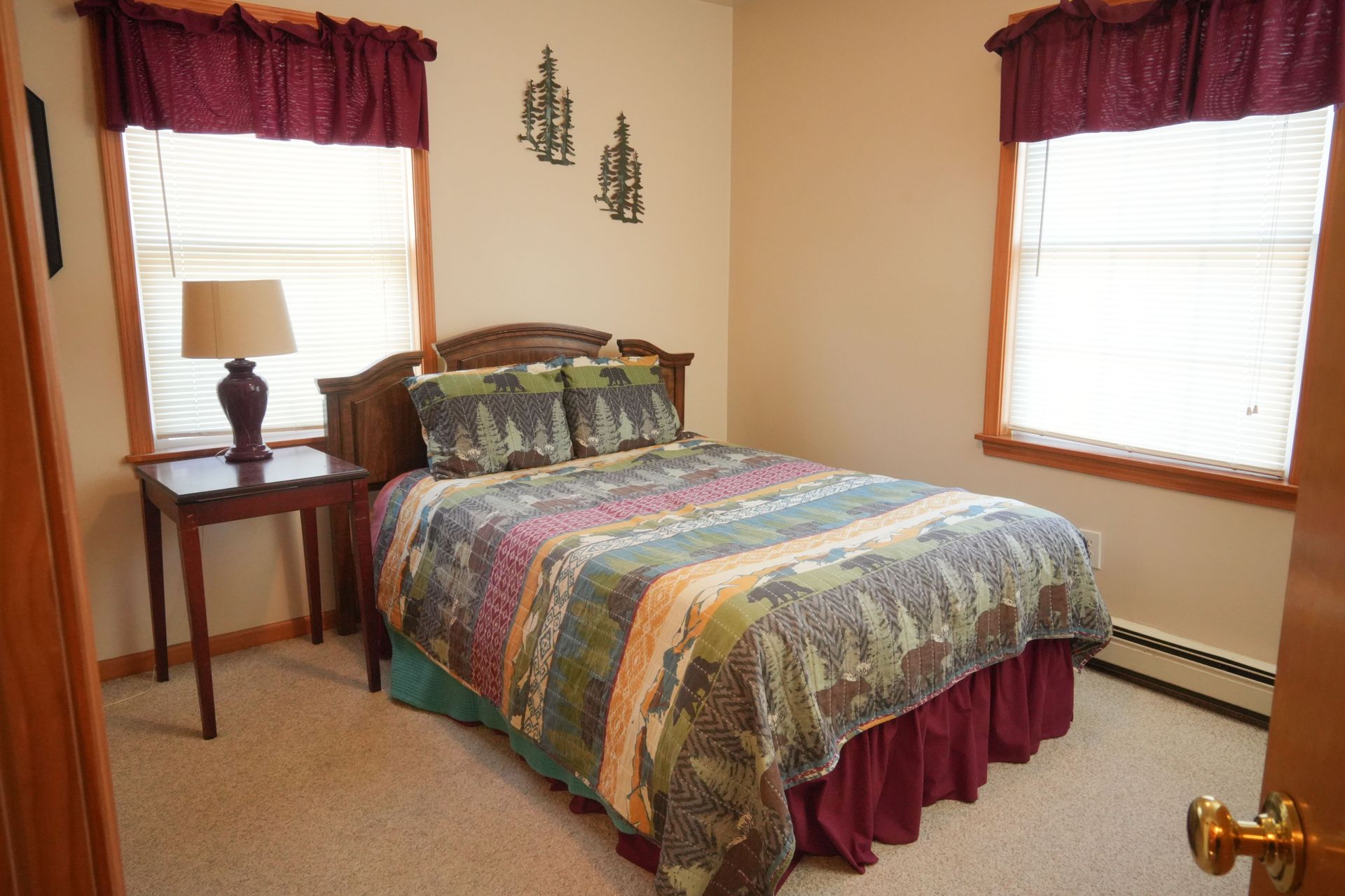 A bedroom with a bed , nightstand , lamp and two windows.