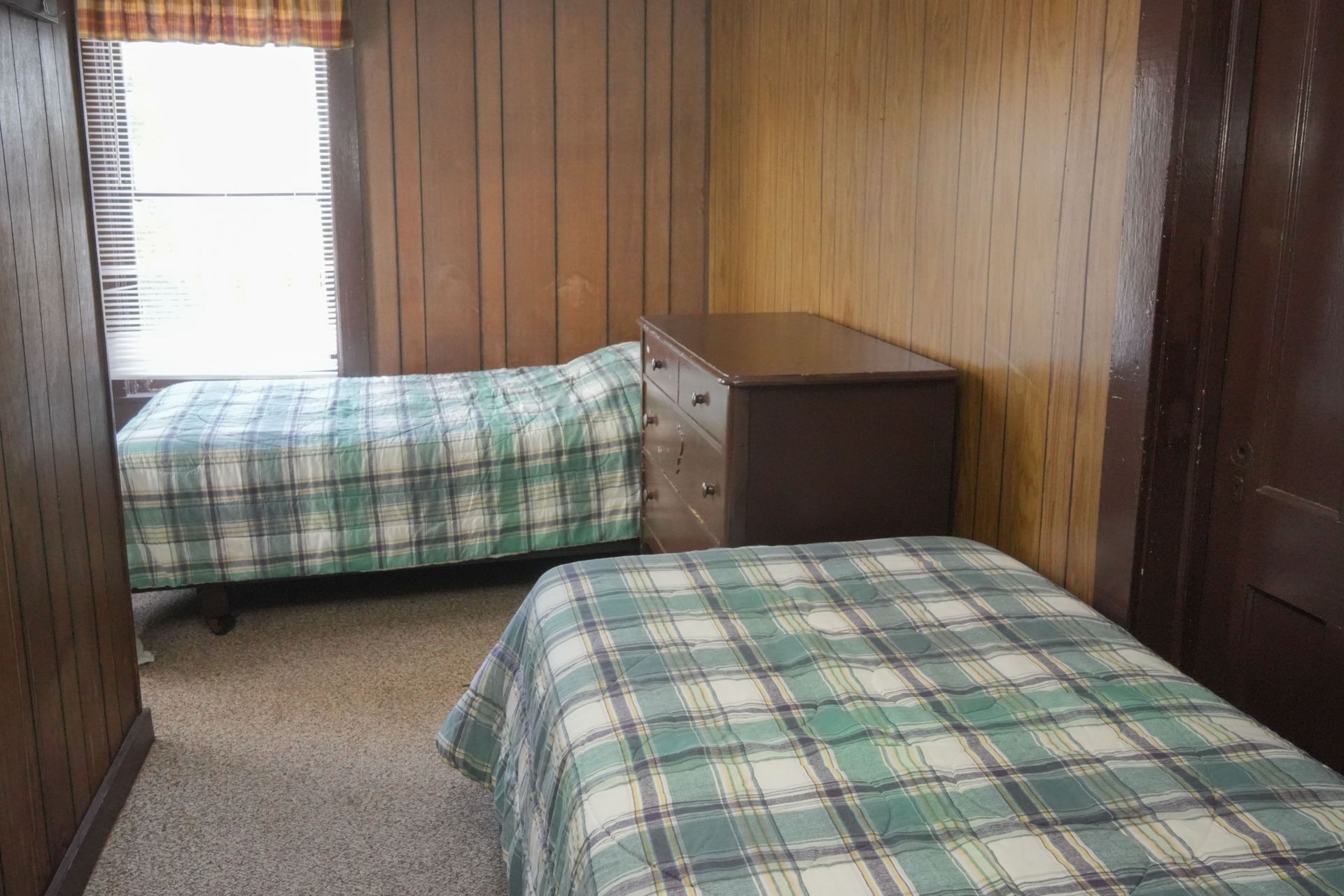 A bedroom with two beds , a dresser and a window.