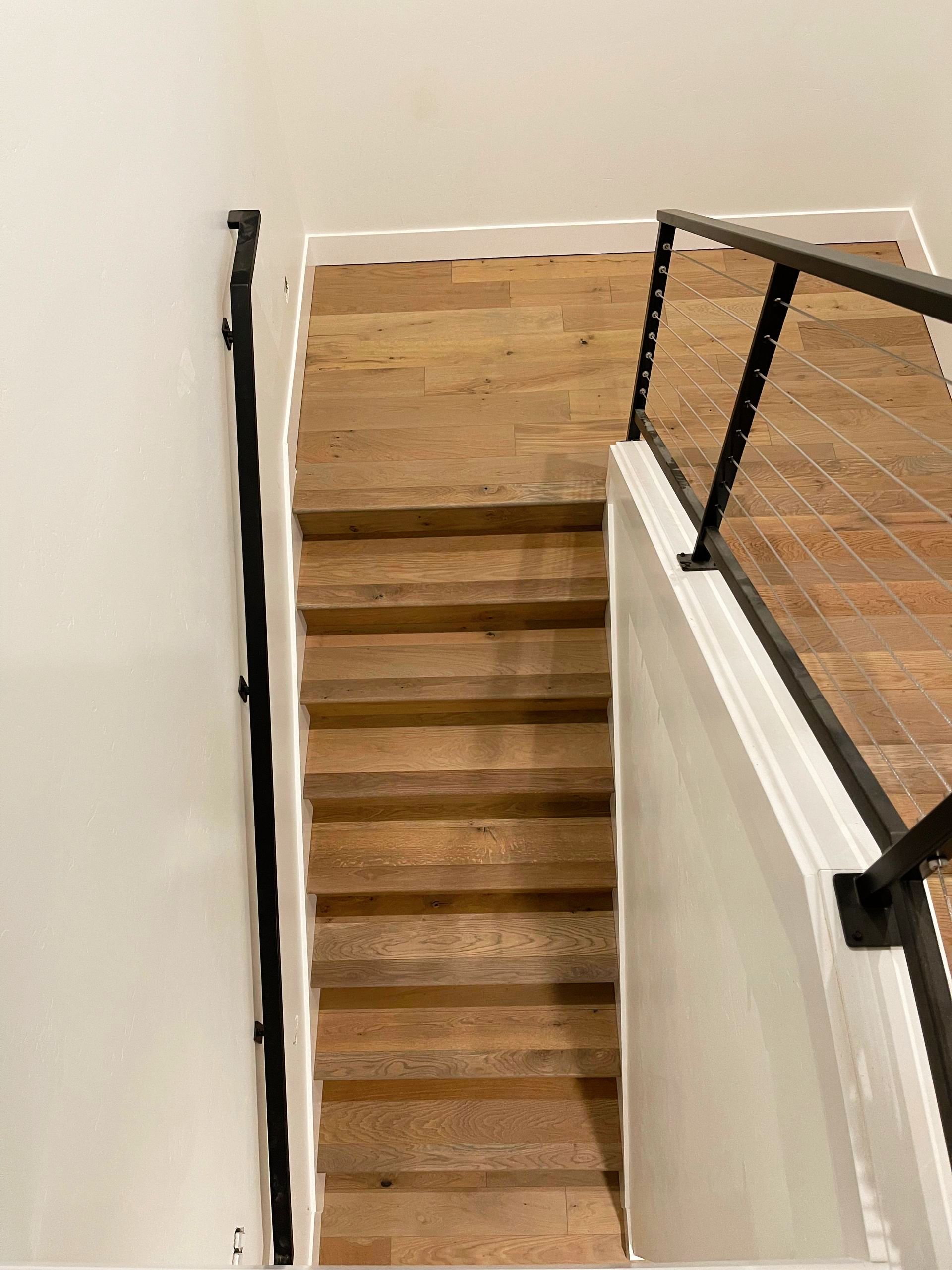 Staircase with wooden steps and black handrails, set in a white-walled interior.