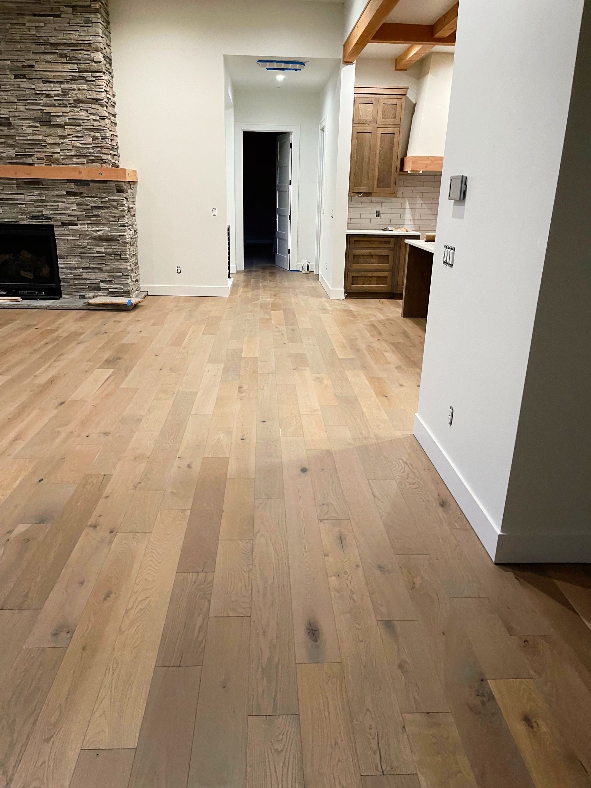 Hardwood floors in a home, leading to a hallway and kitchen. Fireplace on the left.