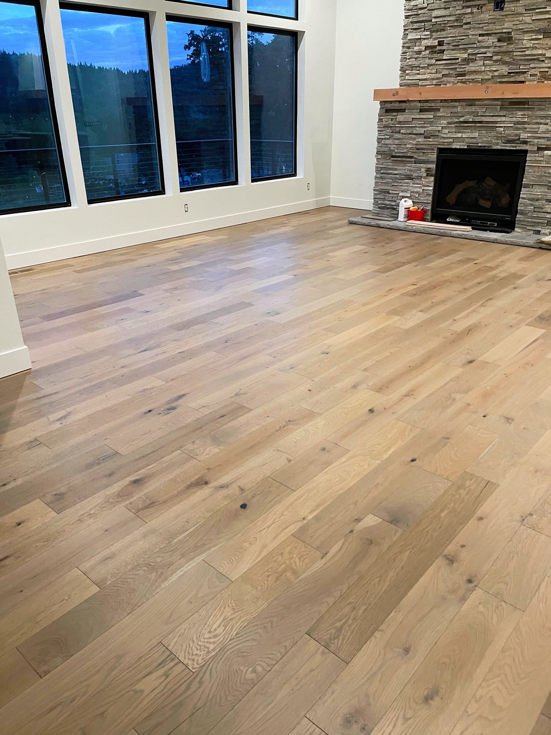 Hardwood floor in a living room with a fireplace and large windows overlooking a body of water.