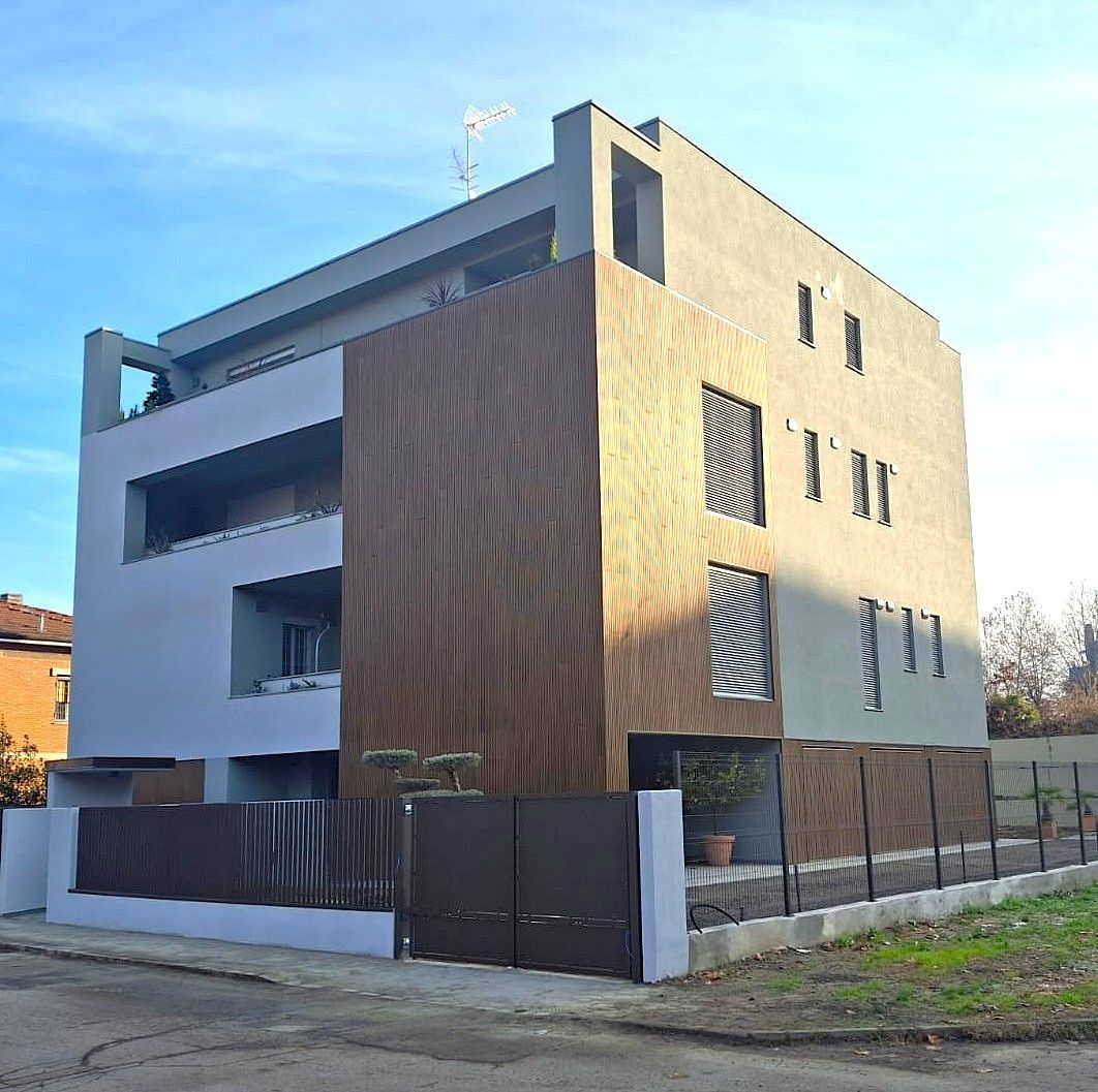 Edificio in stucco giallo con camminamenti in mattoni ad arco sotto un cielo azzurro, circondato da alberi.