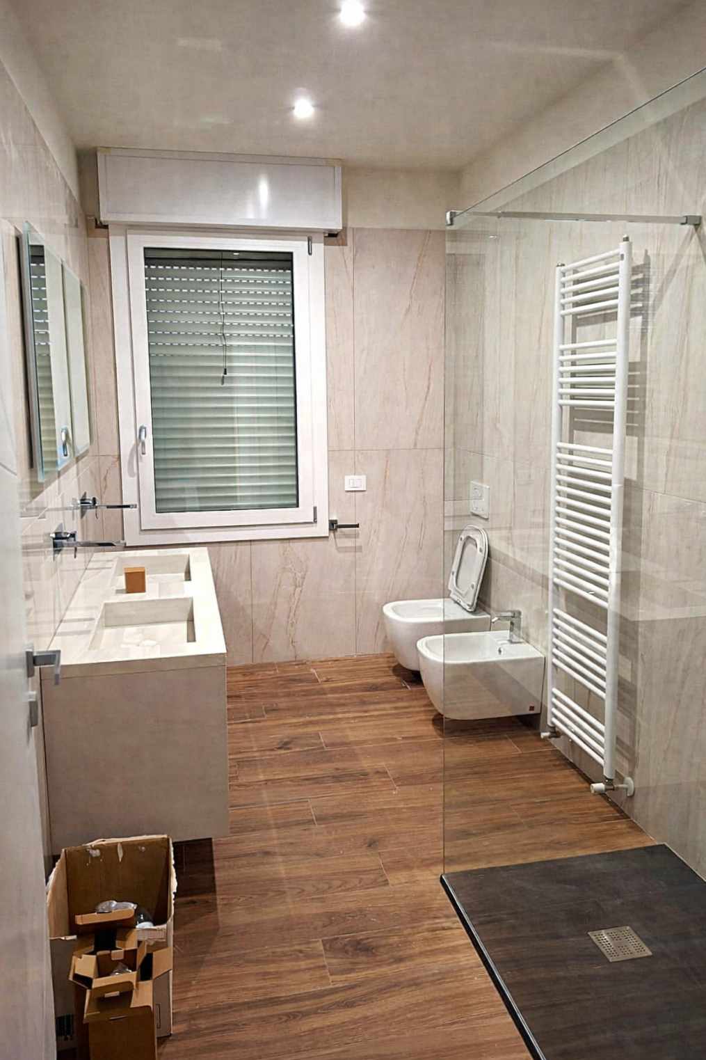 Bagno moderno con pavimento effetto legno, doppio lavabo, doccia, WC e bidet.