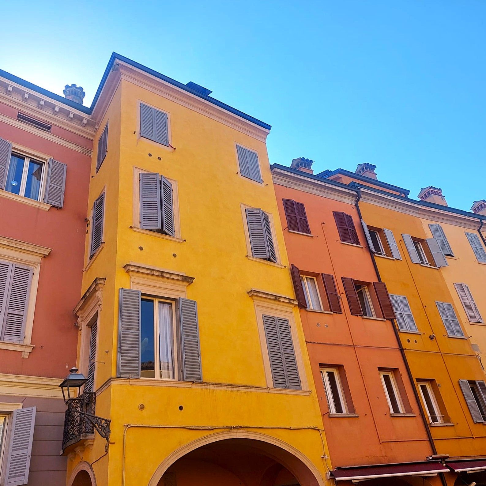 Edifici colorati con ingressi ad arco, persiane e un cielo azzurro e terso.