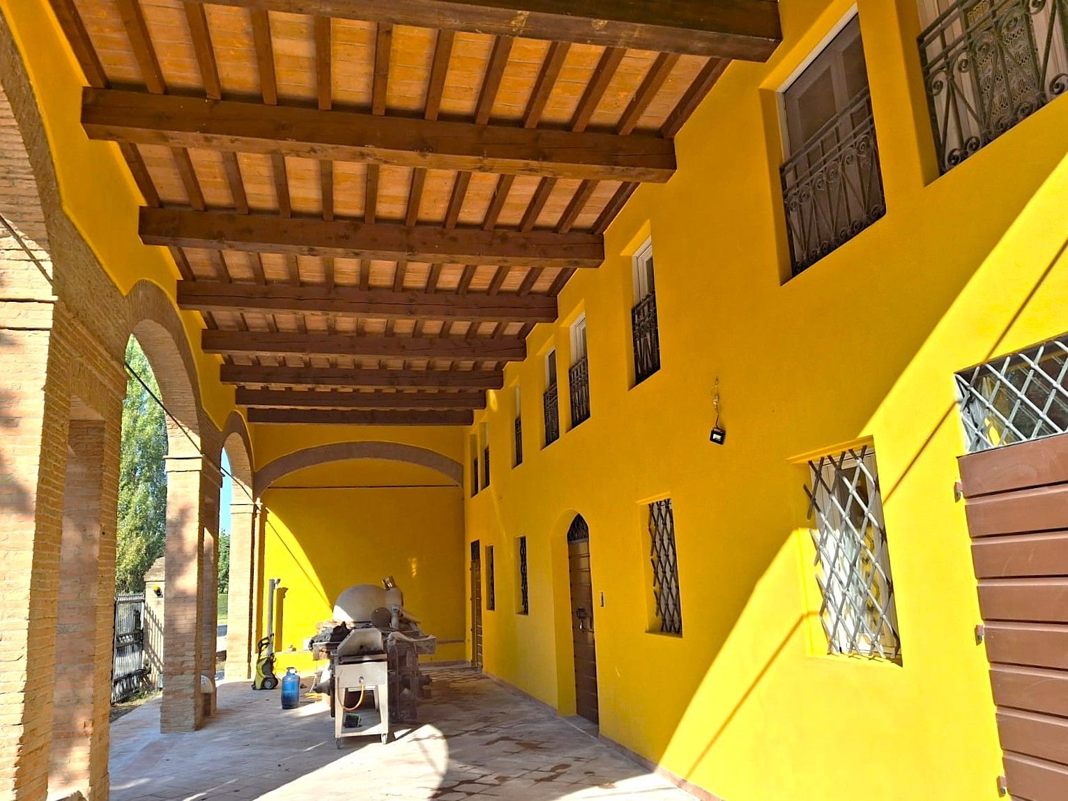 Edificio giallo con travi in legno, portico ad arco e finestre con sbarre.