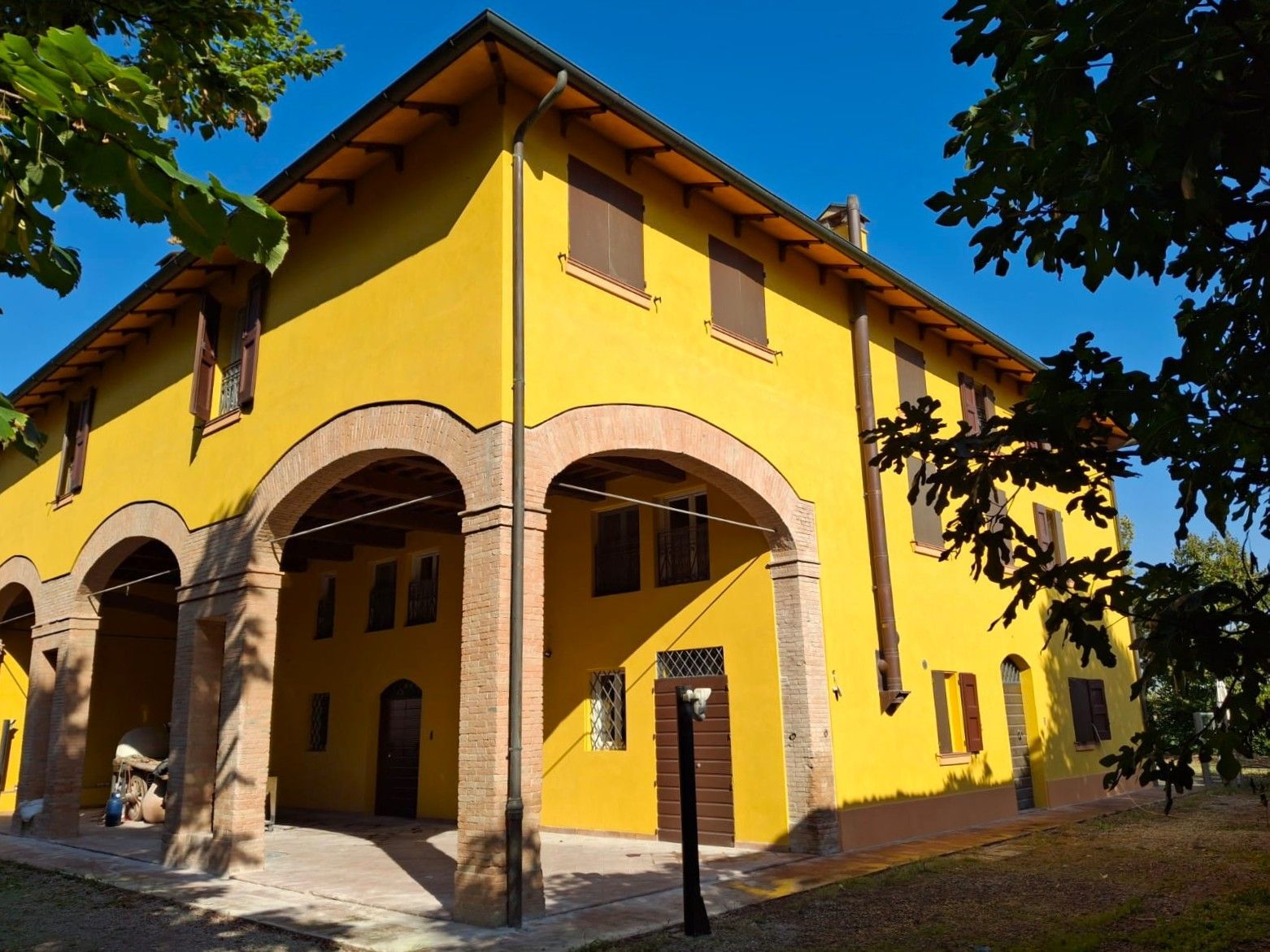 Casa colonica gialla con sostegni ad arco in mattoni sotto un'area coperta; persiane e porta marroni.