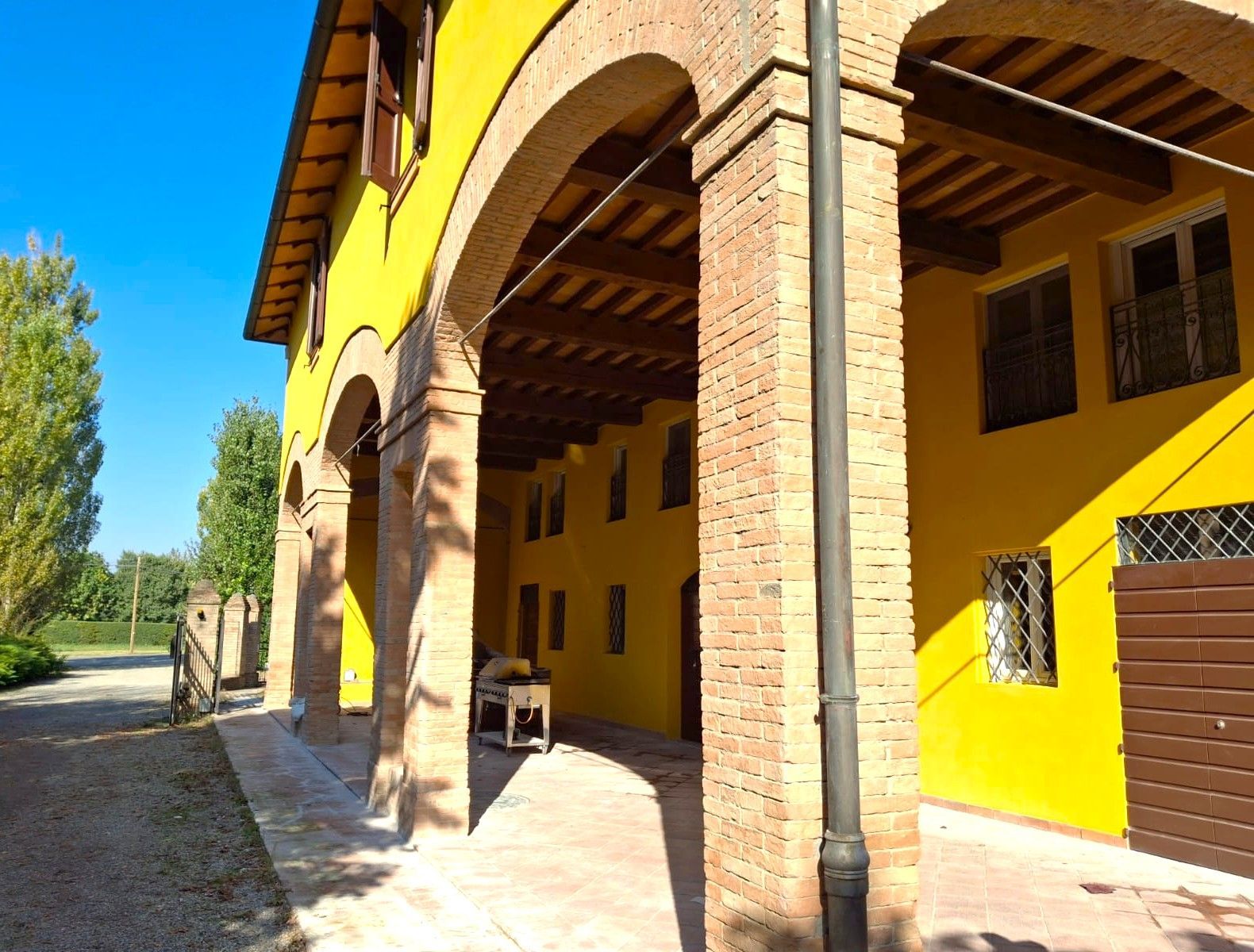 Edificio giallo con archi in mattoni, travi in legno e piccole finestre, vista esterna.