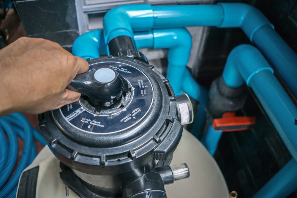 Hand Turning a Black Multiport Valve Connected to Blue Pool Pipes — Ultra Clear Pool Care in Cranbrook, QLD