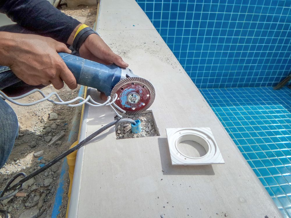 Person Using a Grinder to Cut Concrete Near a Swimming Pool. Blue Tile Is Visible — Ultra Clear Pool Care in Cranbrook, QLD