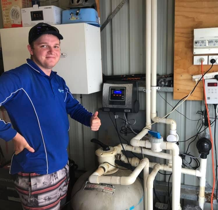 Man Giving Thumbs up Next to Pool Equipment in Shed. He Wears Blue Shirt, Shorts — Ultra Clear Pool Care in Cranbrook, QLD
