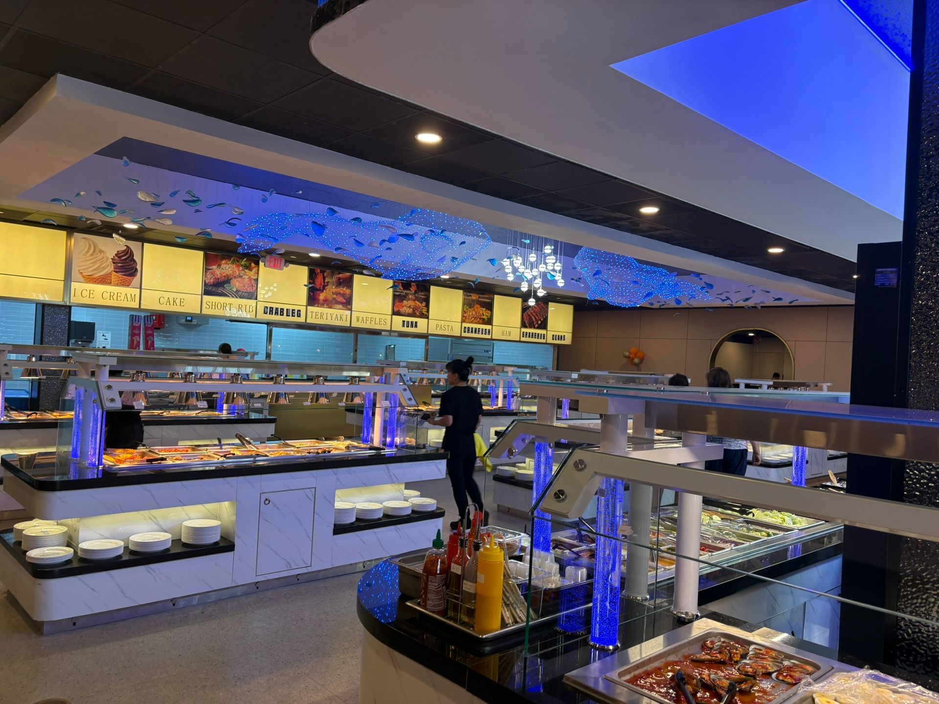 Modern buffet restaurant interior with illuminated counters, white tables, and blue accent lighting