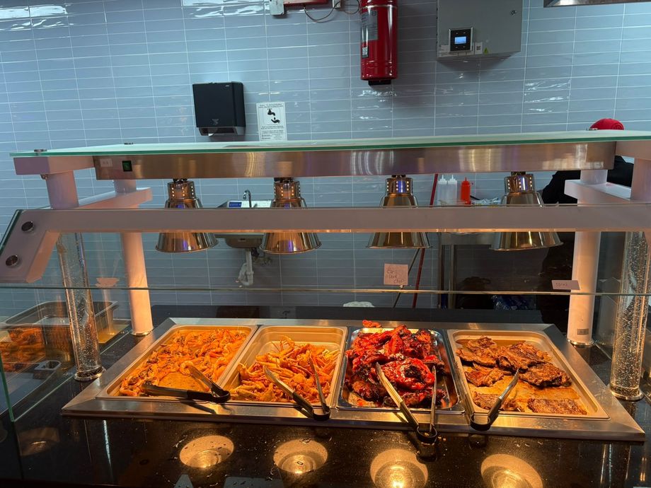Buffet counter with trays of hot food under a glass sneeze guard in a cafeteria or restaurant