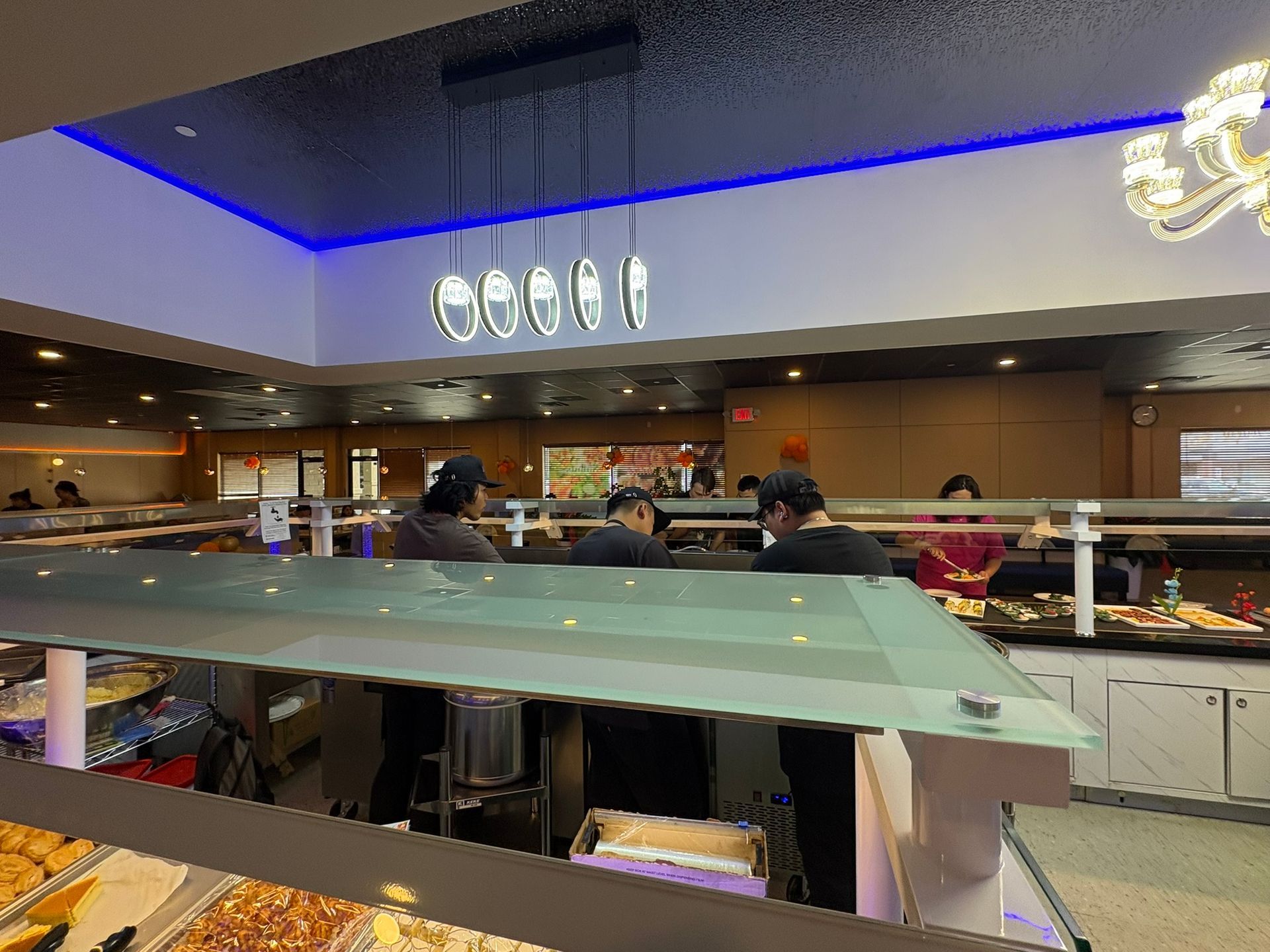 Modern buffet dining area with glass counter, chefs behind a serving station, and blue LED ceiling lights