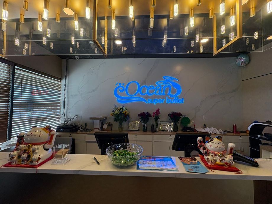 Lobby reception desk with illuminated logo, hanging lights, and potted plants on the counter