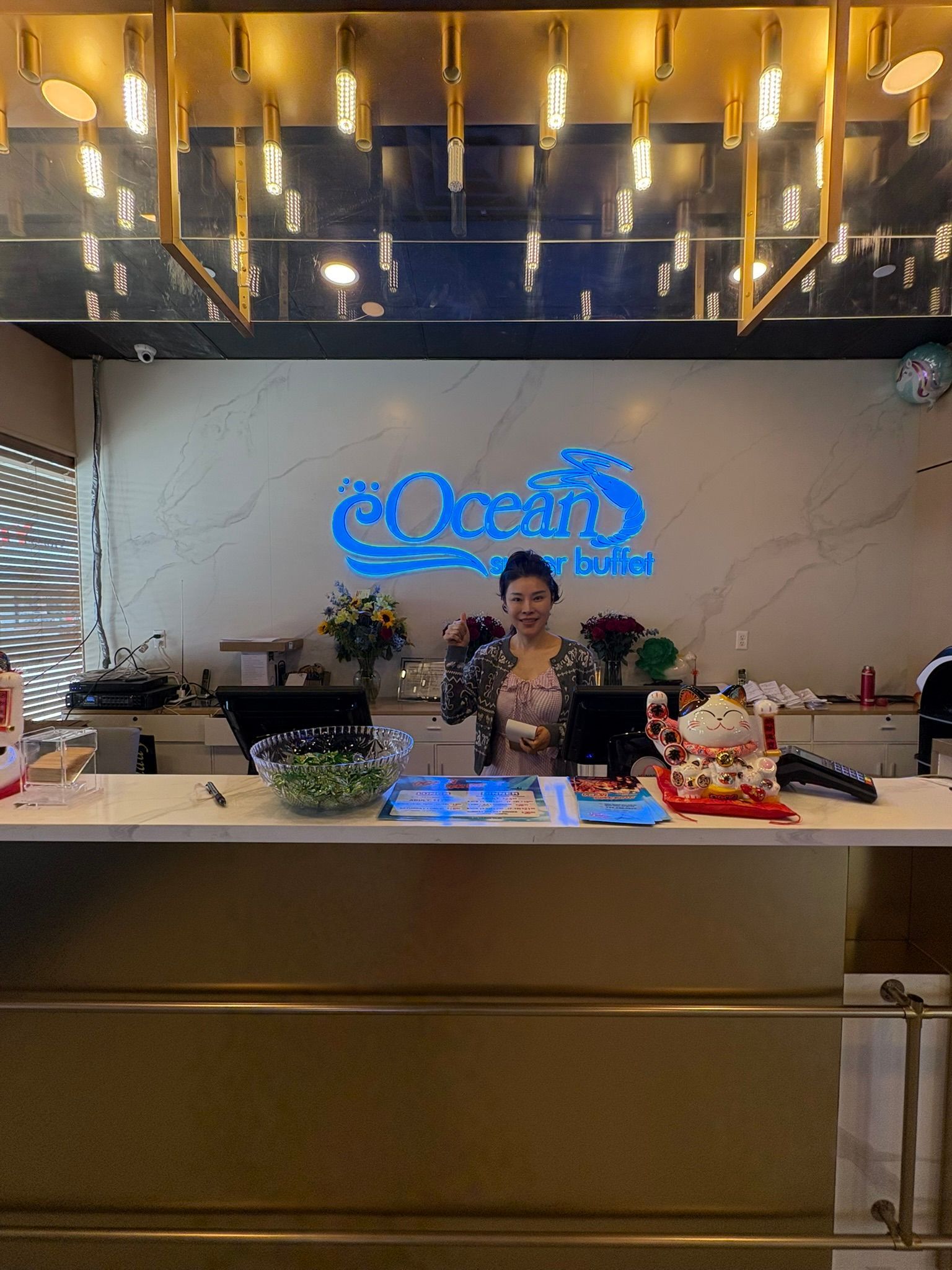 Woman behind a hotel reception desk under a blue neon sign and warm ceiling lights
