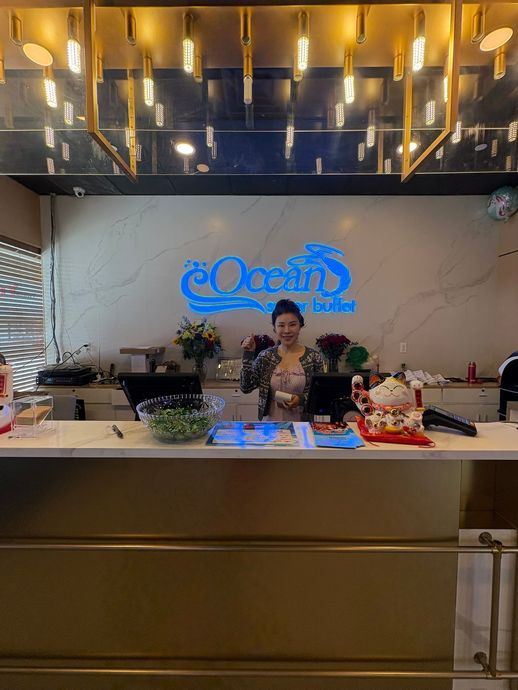 Woman behind a hotel reception desk under a blue neon sign and warm ceiling lights