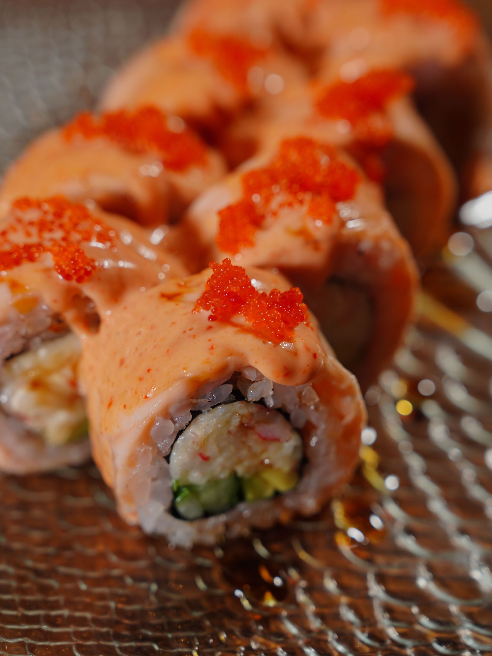 Sushi rolls topped with creamy sauce and red roe on a textured plate