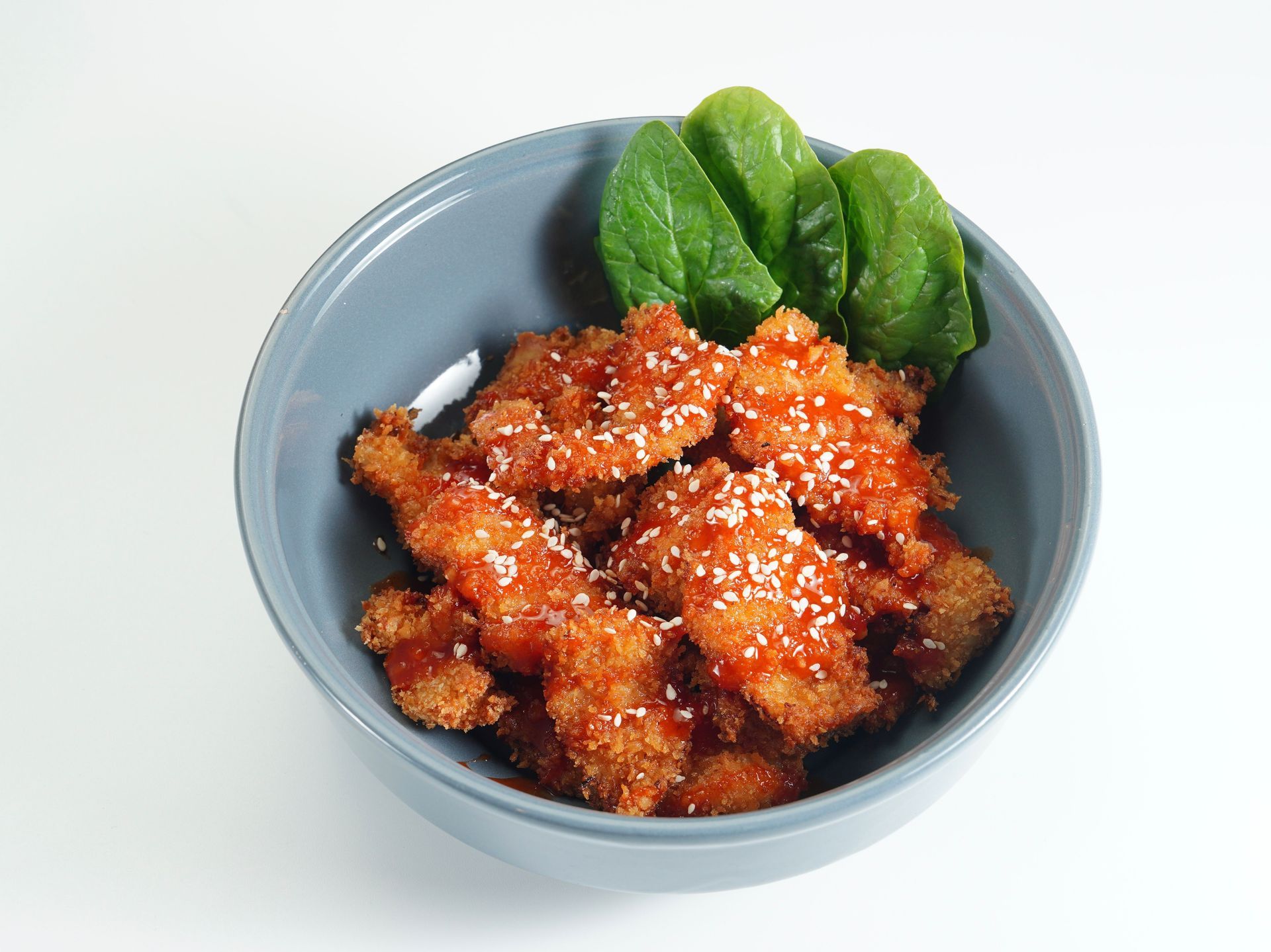 Bowl of glazed fried chicken pieces with green garnish on a white background
