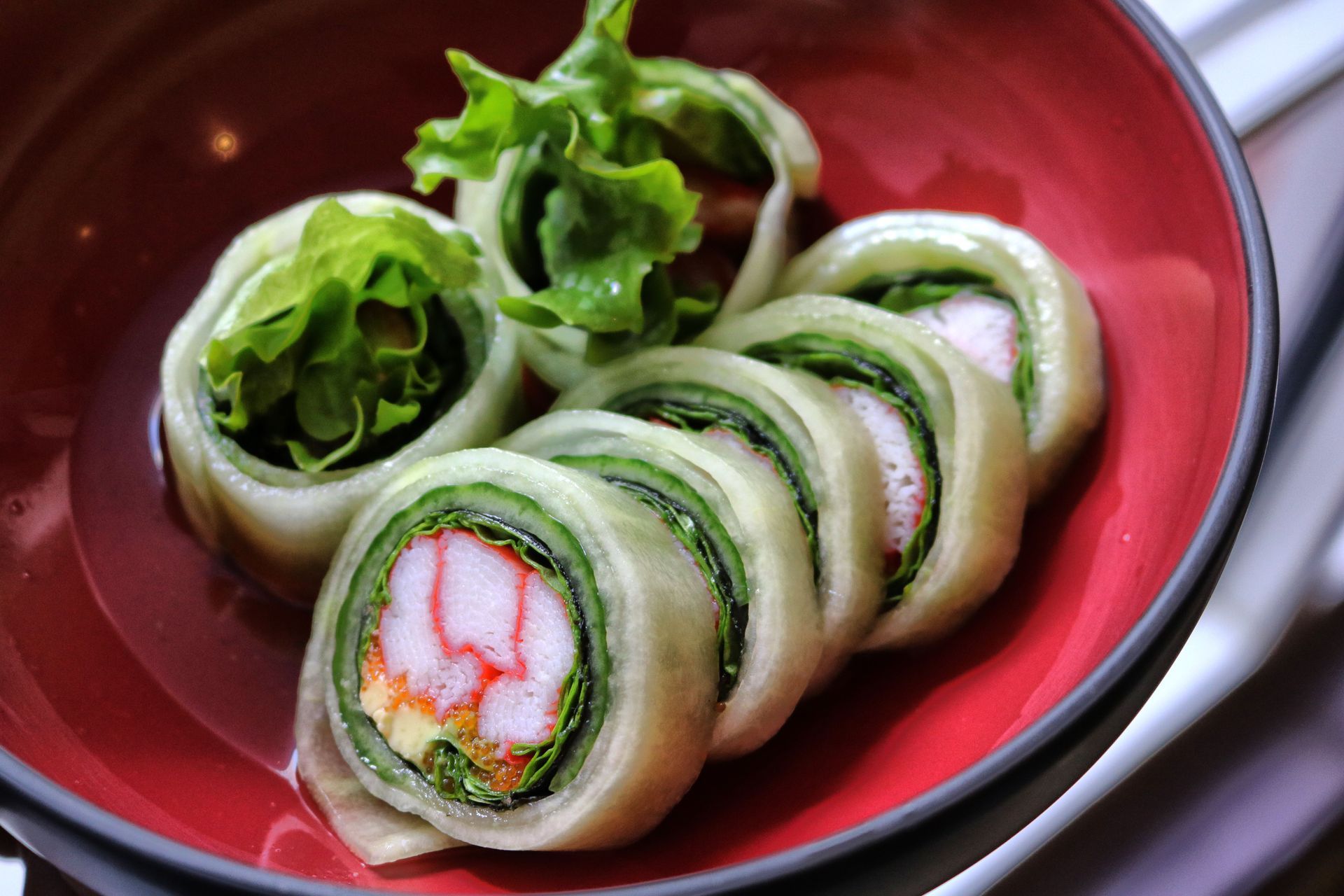 Sliced cucumber and crab sushi rolls on a red plate