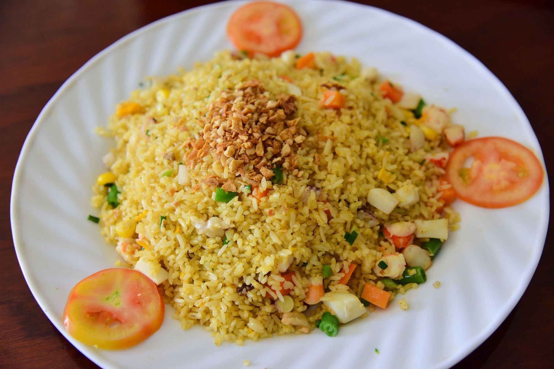 Plate of yellow rice with mixed vegetables and tomato slices on a white dish