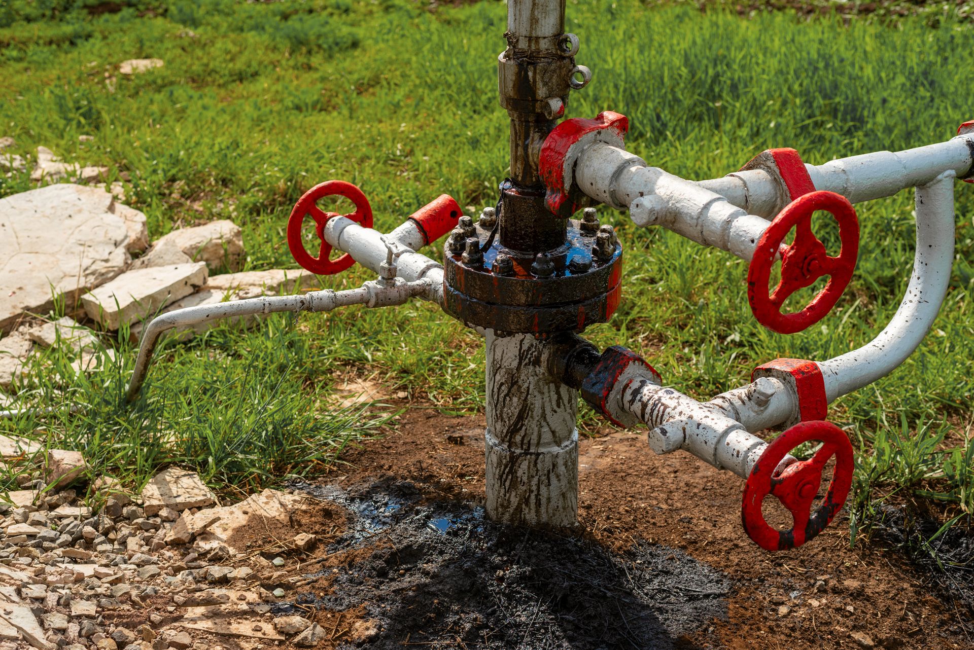 A close up of a pipe with red valves on it in a field.
