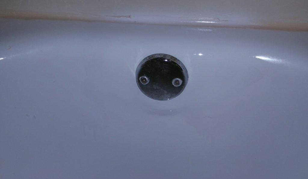A close up of a bathtub drain with water coming out of it.