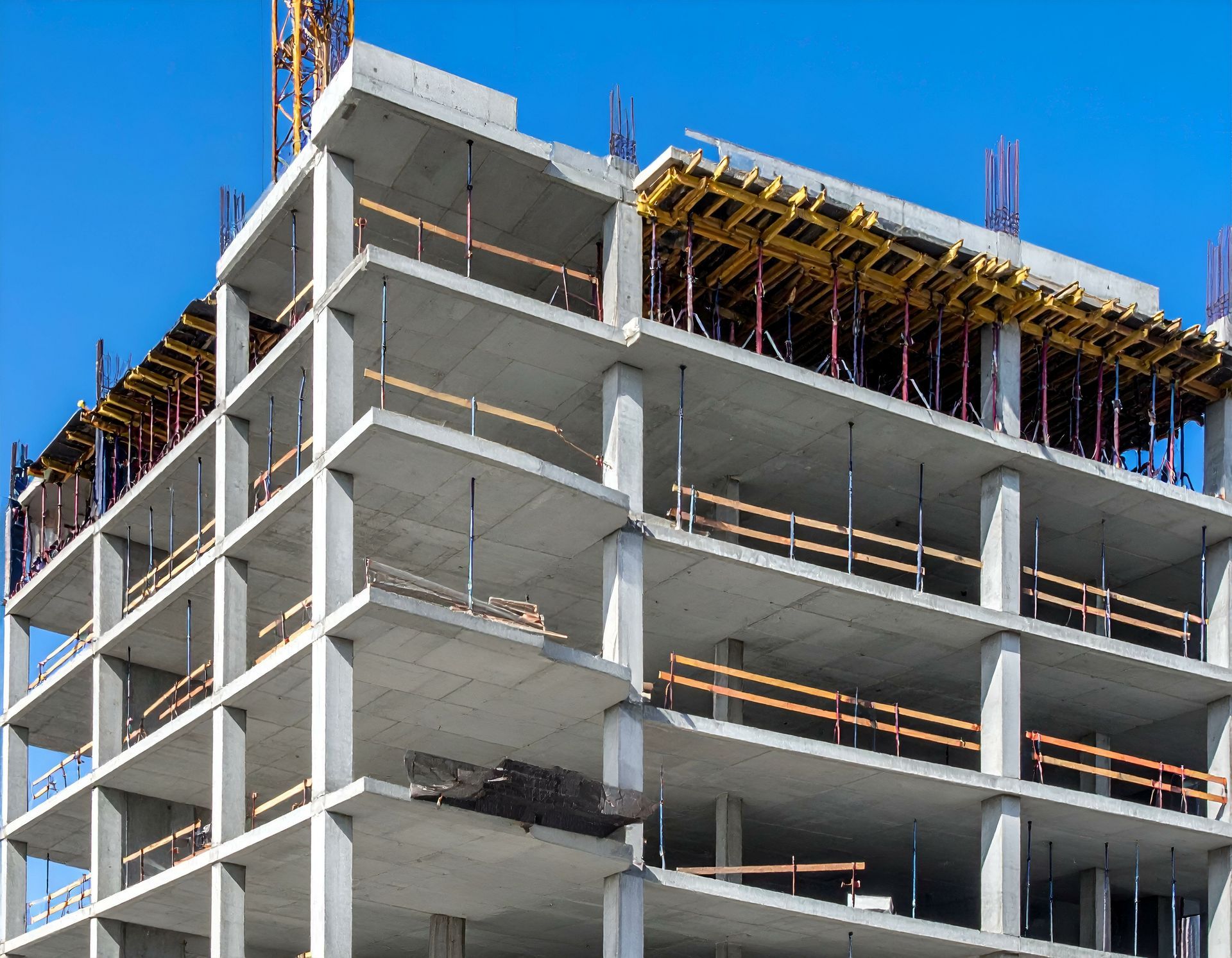 Chantier de construction d'un immeuble à plusieurs étages avec sols en béton, colonnes de soutien et garde-corps de sécurité contre un ciel bleu.