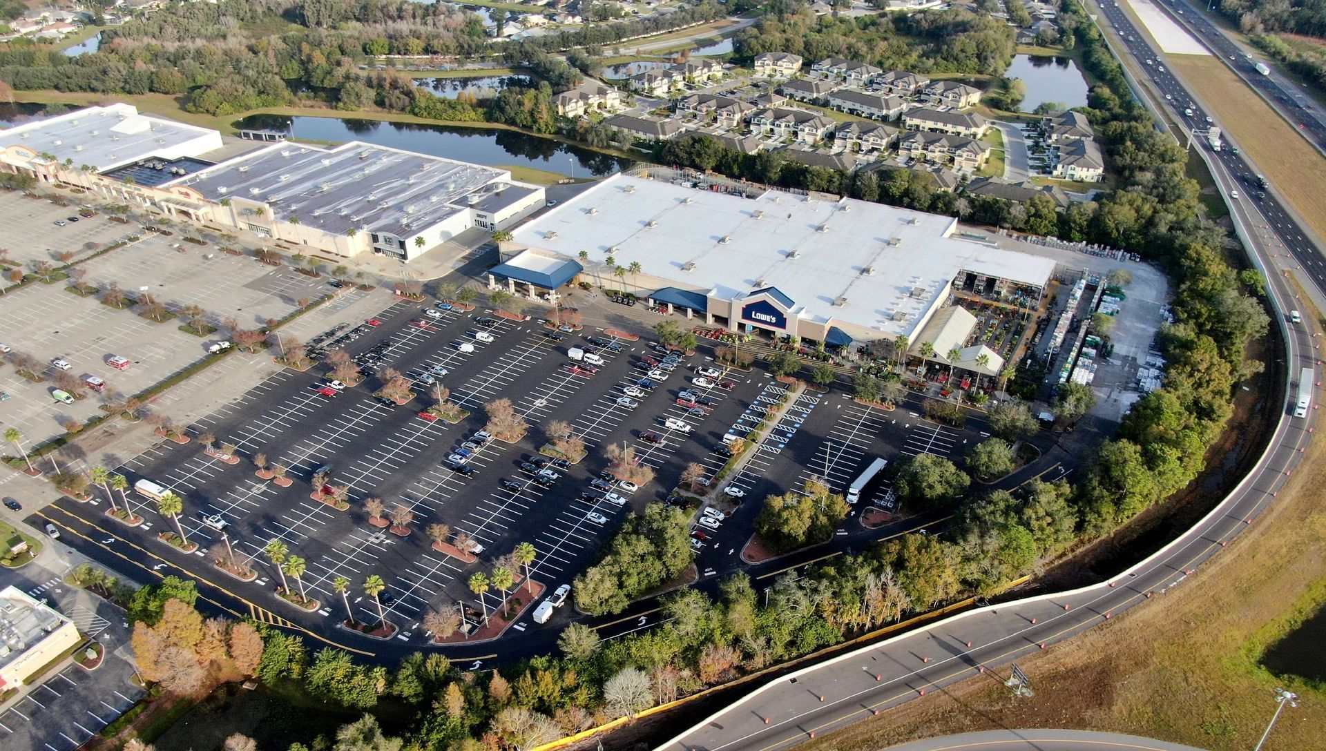 Aerial view of a large industrial complex with parking lots, warehouses, and a curved road beside trees
