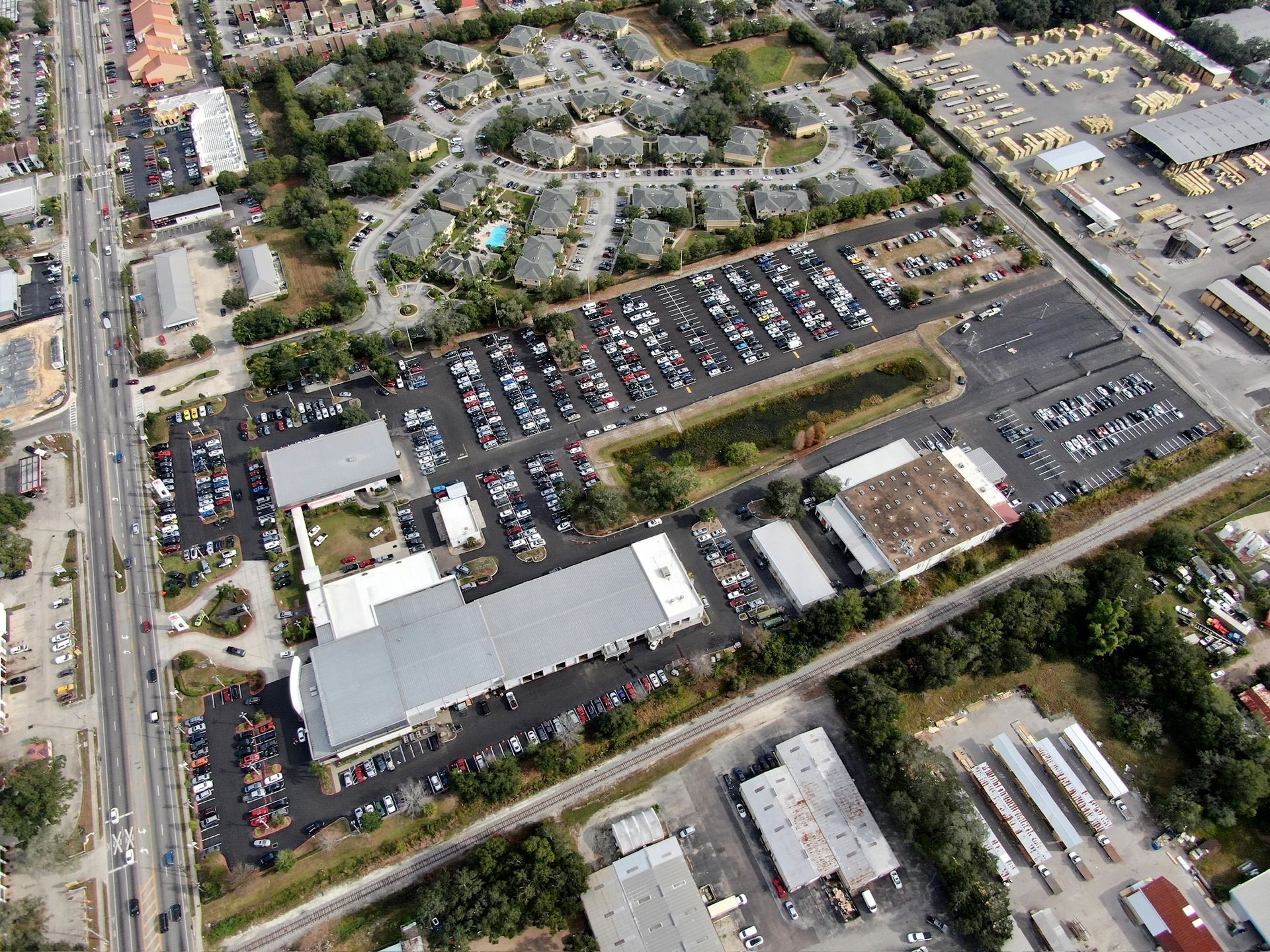 Aerial view of a suburban shopping center with parking lots, stores, and surrounding trees and roads.