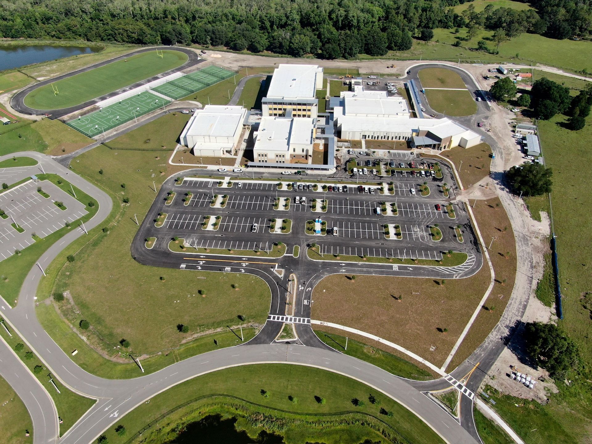 Aerial view of a large building complex with parking lots, roads, and surrounding green fields.