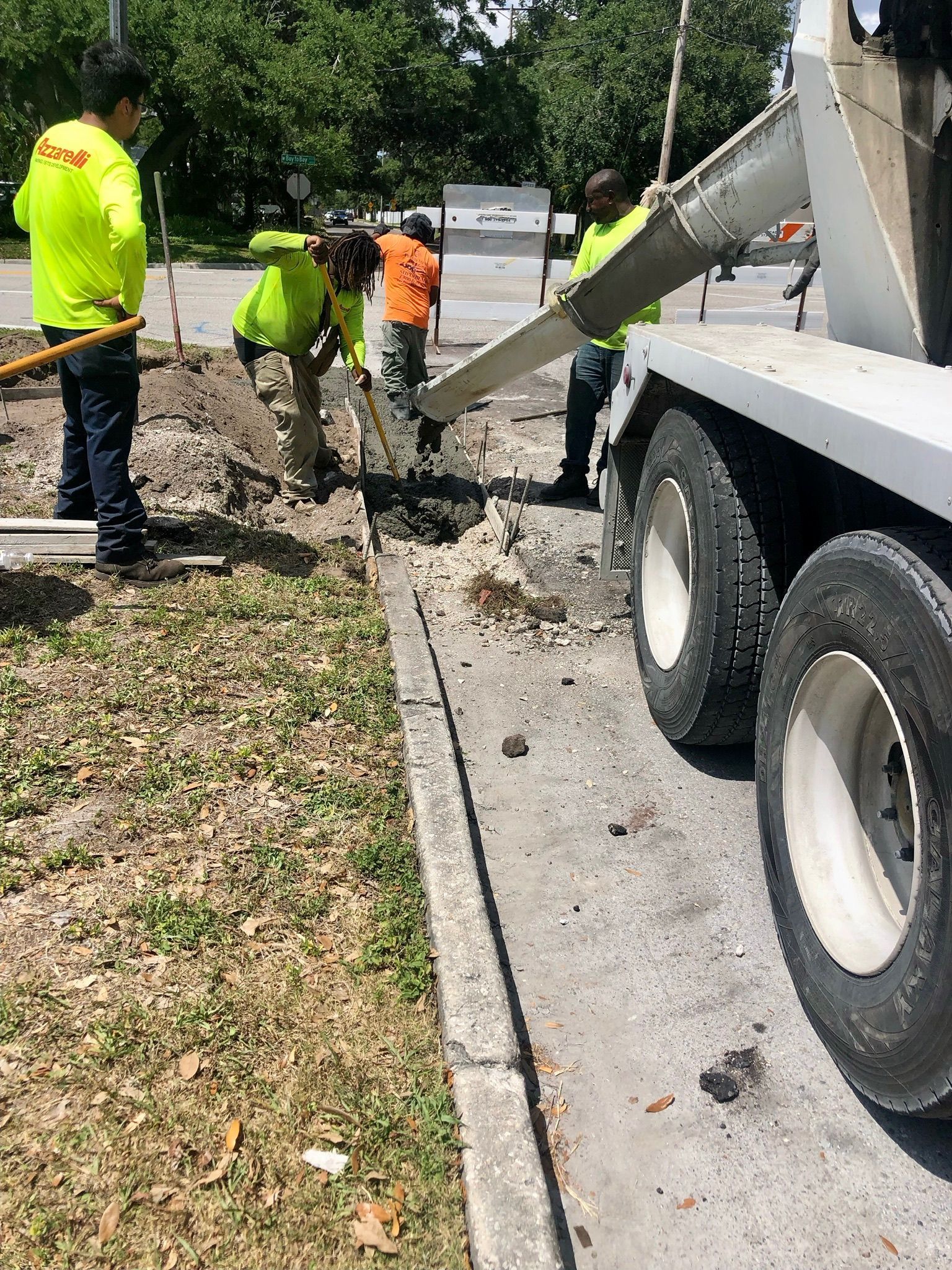 Workers repair a roadside trench beside a concrete truck on a sunny street.