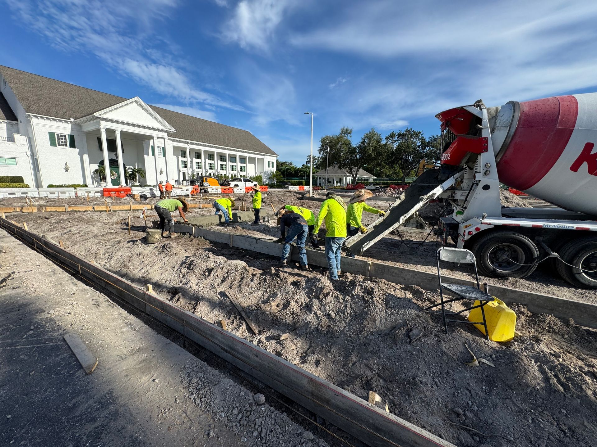 Construction crew pouring concrete at a building site beside a red cement mixer truck.