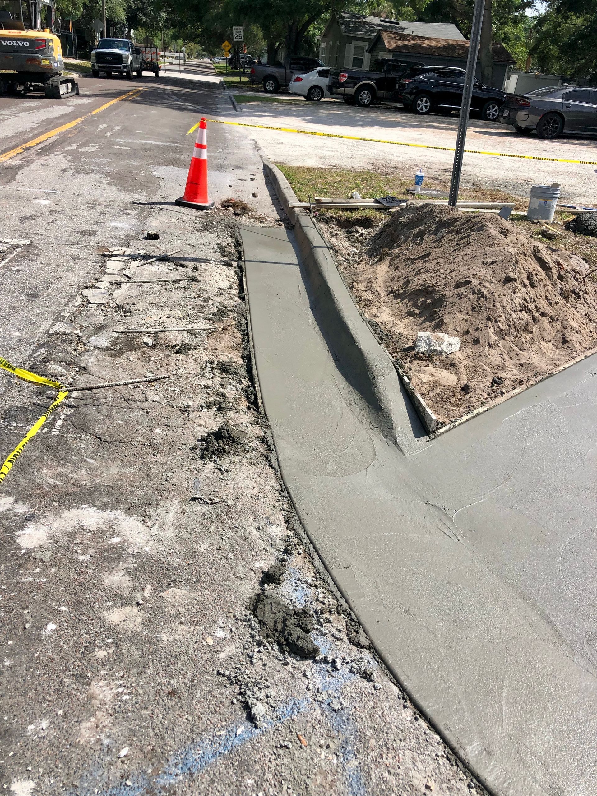 Damaged sidewalk curb ramp under repair with fresh concrete and orange cone beside a street construction area
